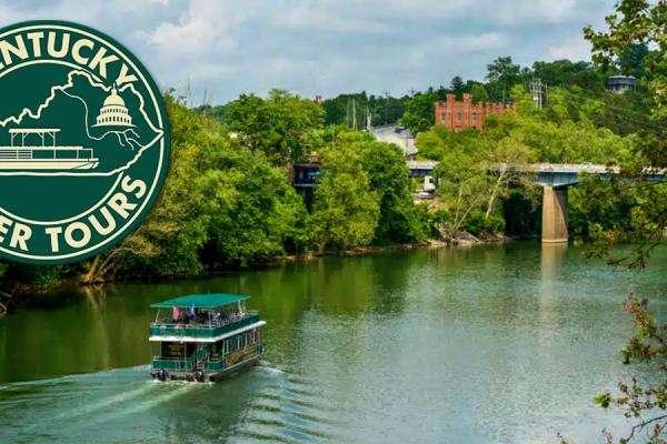 Kentucky River in Frankfort Kentucky. A Kentucky Bourbon River Tour boat can be seen moving towards a bridge in the distance, with a distillery also in the distance.